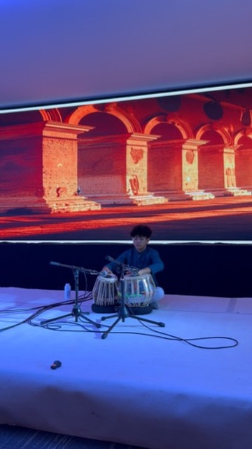 Young student performing a tabla solo beneath a traditional stage backdrop